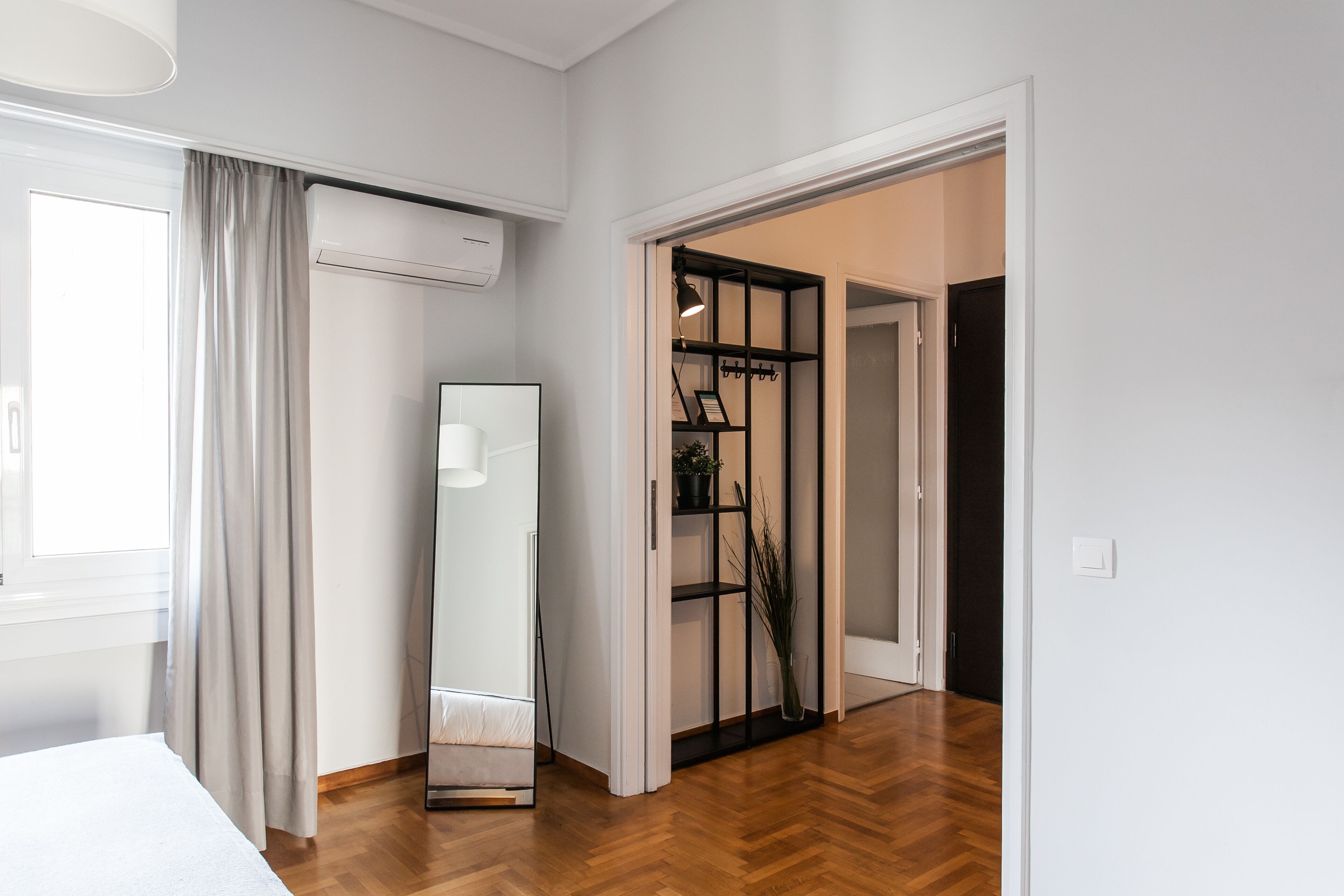 Una habitación de hotel con una cama, un espejo grande, un armario y suelo de madera.