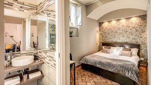 A modern bathroom with a large mirror, a round sink, and a vanity with shelves. The bedroom features a large bed with a patterned bedspread, a headboard, and a brick floor. - Maison Babuino with a panoramic terrace (Roma)