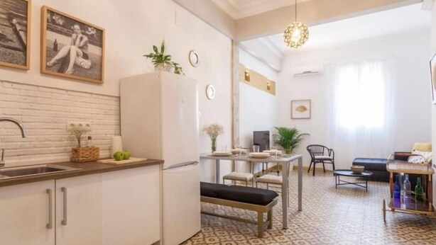 Una cocina compacta con armarios blancos, un refrigerador y un comedor con un banco.