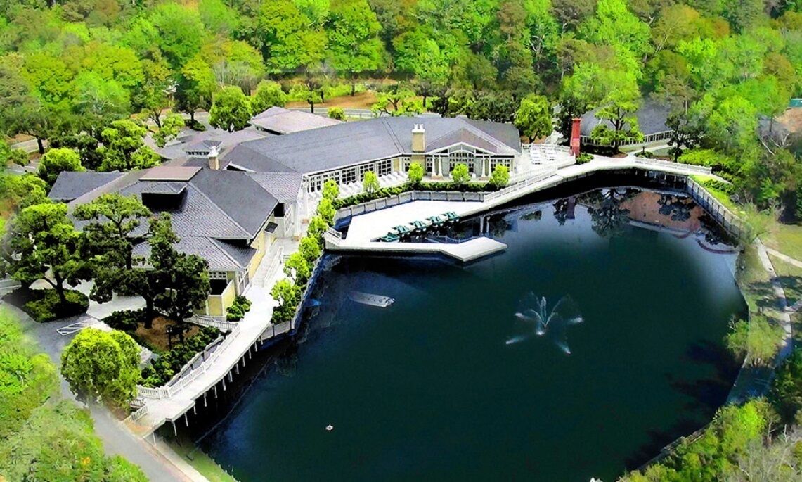 An aerial view of a lakeside property with a large house, a dock, and surrounding greenery.