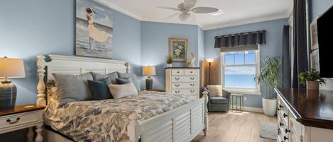 A bedroom with a bed, nightstands, a dresser, a ceiling fan, a window with curtains, and a painting on the wall.