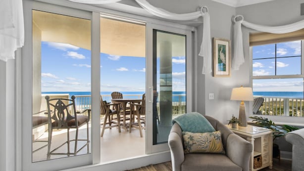 A balcony with a view of the ocean, a sofa, a table with a lamp, and a framed picture on the wall.