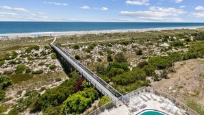 A beach view with a pier, a pool area, and a sandy landscape.