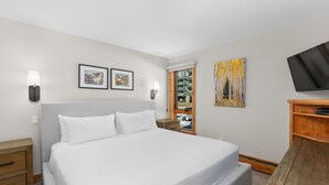 A hotel room with a large bed, two wall-mounted lamps, a flat-screen TV, and a wooden side table. - Vail 21 303 - 2 Bedroom Platinum (Vail)