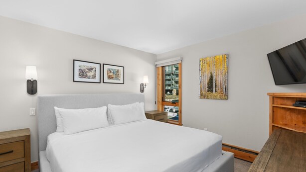 A hotel room with a large bed, two wall-mounted lamps, a flat-screen TV, and a wooden side table. - Vail 21 303 - 2 Bedroom Platinum (Vail)