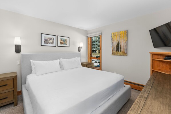 A hotel room with a large bed, two wall-mounted lamps, a flat-screen TV, and a wooden side table. - Vail 21 303 - 2 Bedroom Platinum (Vail)