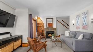 A modern living room with a grey sofa, wooden armchairs, a coffee table, and a flat-screen TV mounted on the wall. - Vail 21 303 - 2 Bedroom Platinum (Vail)