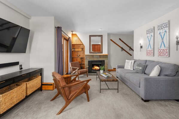 A modern living room with a grey sofa, wooden armchairs, a coffee table, and a flat-screen TV mounted on the wall. - Vail 21 303 - 2 Bedroom Platinum (Vail)