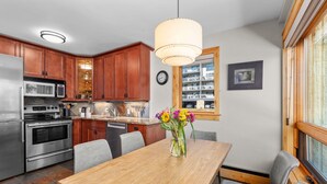 A modern kitchen with wooden cabinets, stainless steel appliances, and a dining area with a wooden table and chairs. - Vail 21 303 - 2 Bedroom Platinum (Vail)