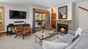 A modern living room with a fireplace, comfortable seating, a flat-screen TV, and a large window. - Vail 21 303 - 2 Bedroom Platinum (Vail)