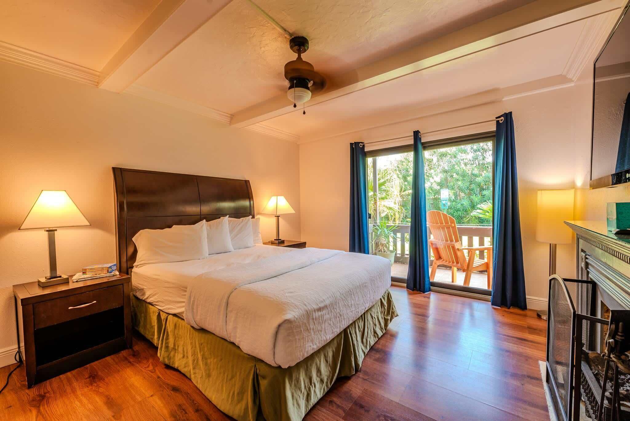 Une chambre d’hôtel avec un grand lit, deux tables de chevet avec des lampes, un ventilateur de plafond et une vue sur l’extérieur grâce à une porte-fenêtre coulissante.