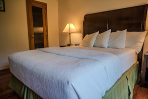 A neatly made bed with a headboard, a bedside lamp, and a nightstand with a book. - Toucans Retreat  (South Padre Island)