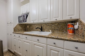 A kitchen with white cabinets, a granite countertop, a stainless steel sink, a black faucet, and a microwave. - Toucans Retreat  (South Padre Island)