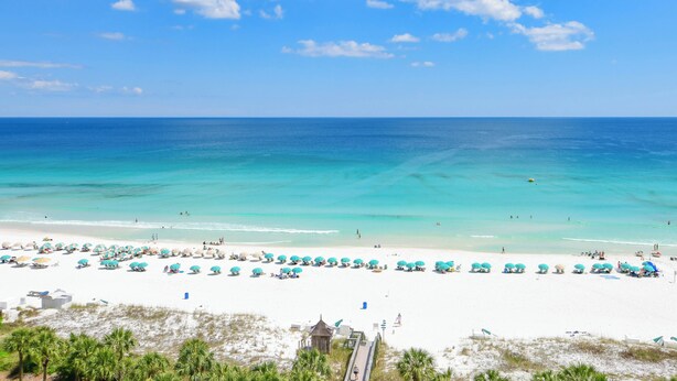 Een strand met wit zand, turquoise water en een rij blauwe parasols.