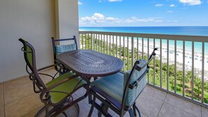 Een balkon met een tafel en stoelen, met uitzicht op een strand en heldere lucht.