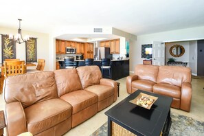 A living room with a brown leather sofa, a black coffee table, and a dining area with wooden chairs and a chandelier.