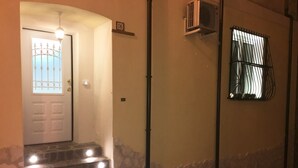 Een trap die leidt naar een deur met een nummerbord, een raam met tralies, en een airconditioner aan de muur.