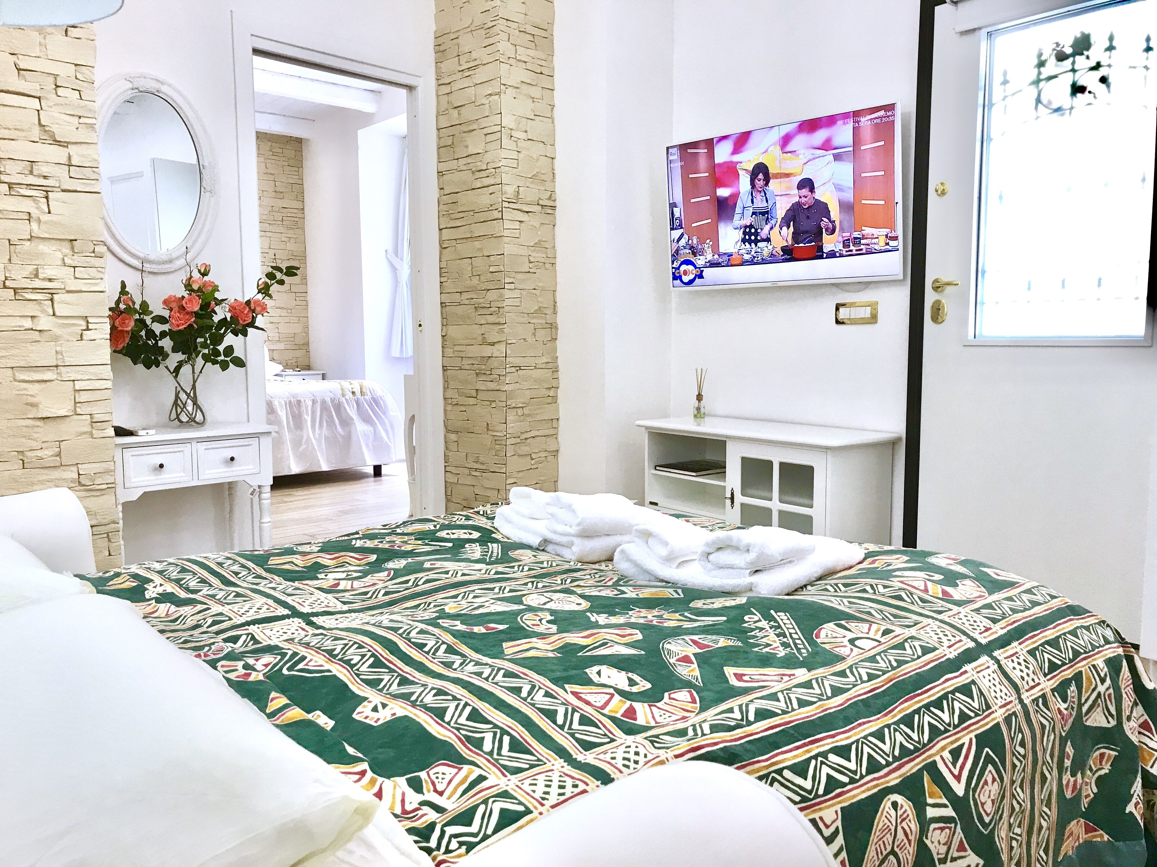 A hotel room with a bed, a dresser, a mirror, a television, and a door leading to another room.