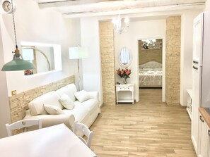 A room with a white sofa, a small white table with a vase of flowers, a mirror, and a bed in the background. - Casanova Luxury-Apartment (Vibo Valentia)