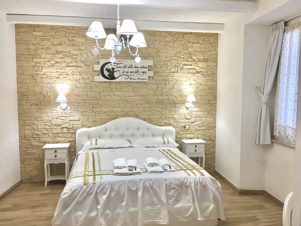A bedroom with a stone-patterned wall, a white bed with gold accents, bedside lamps, and a quote sign. - Casanova Luxury-Apartment (Vibo Valentia)