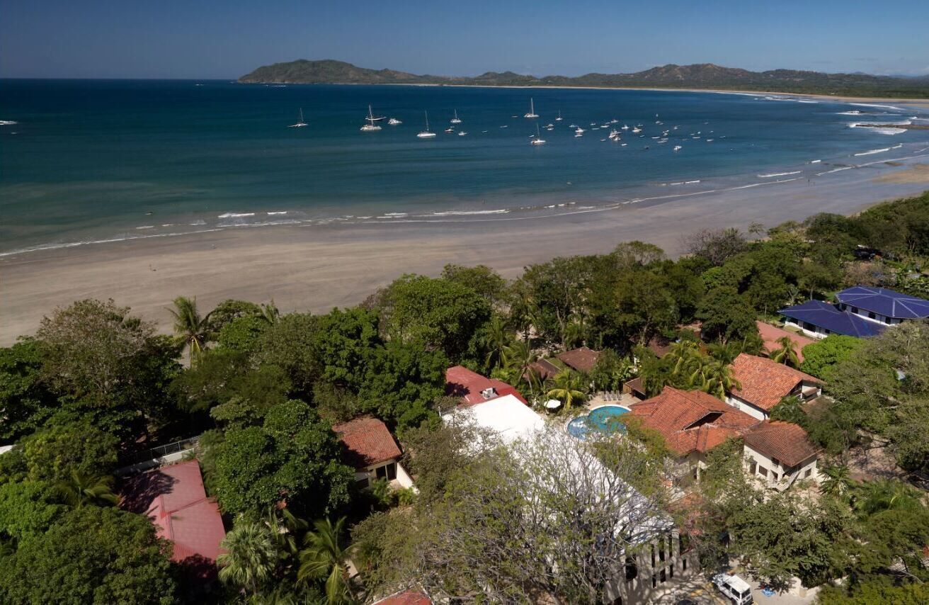 Una propiedad costera con vista a la playa, casas con techos rojos y una piscina.