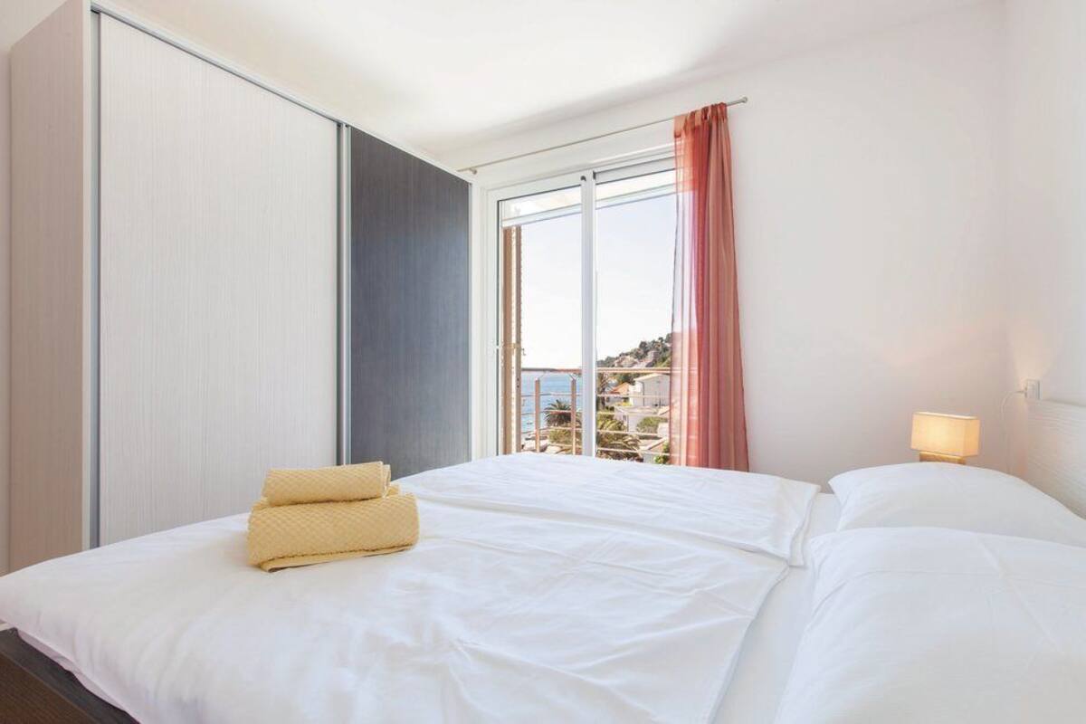 A hotel room with a bed, a nightstand, a window with curtains, and a view of the outside.