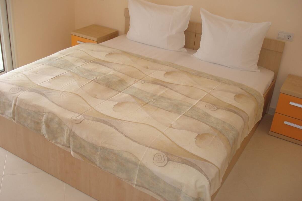 A neatly made bed with a patterned bedspread, two pillows, and a nightstand with a drawer.