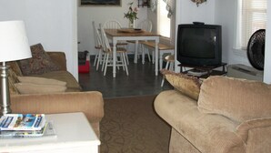 A living room with a television, a dining table with chairs, a couch, and a lamp.