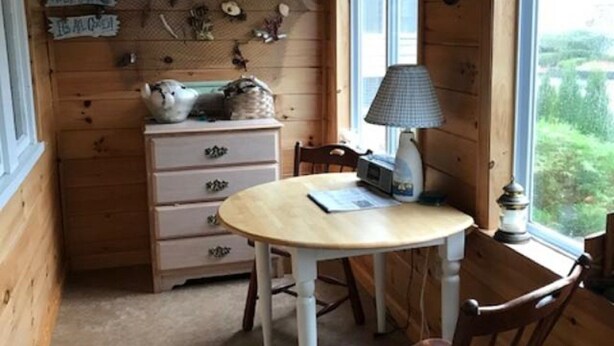 A wooden interior with a round table and chairs, a lamp, and a dresser with drawers.