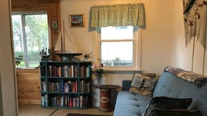 A cozy living room with a blue sofa, a bookshelf, and a window with a view.