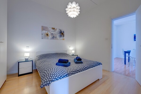 A bedroom with a bed, bedside tables, a wall-mounted light fixture, and a painting.