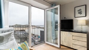 Un balcón con vista a la playa y edificios, un televisor, una lámpara y un aparador de mármol.