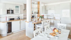 Una cocina moderna con armarios blancos, horno empotrado y comedor con mesa dispuesta para el desayuno.