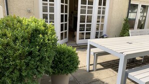 A patio area with a white table and chairs, a potted plant, and a building entrance with glass doors. - Georgian House with Indoor Swimming Pool (Willsbridge)