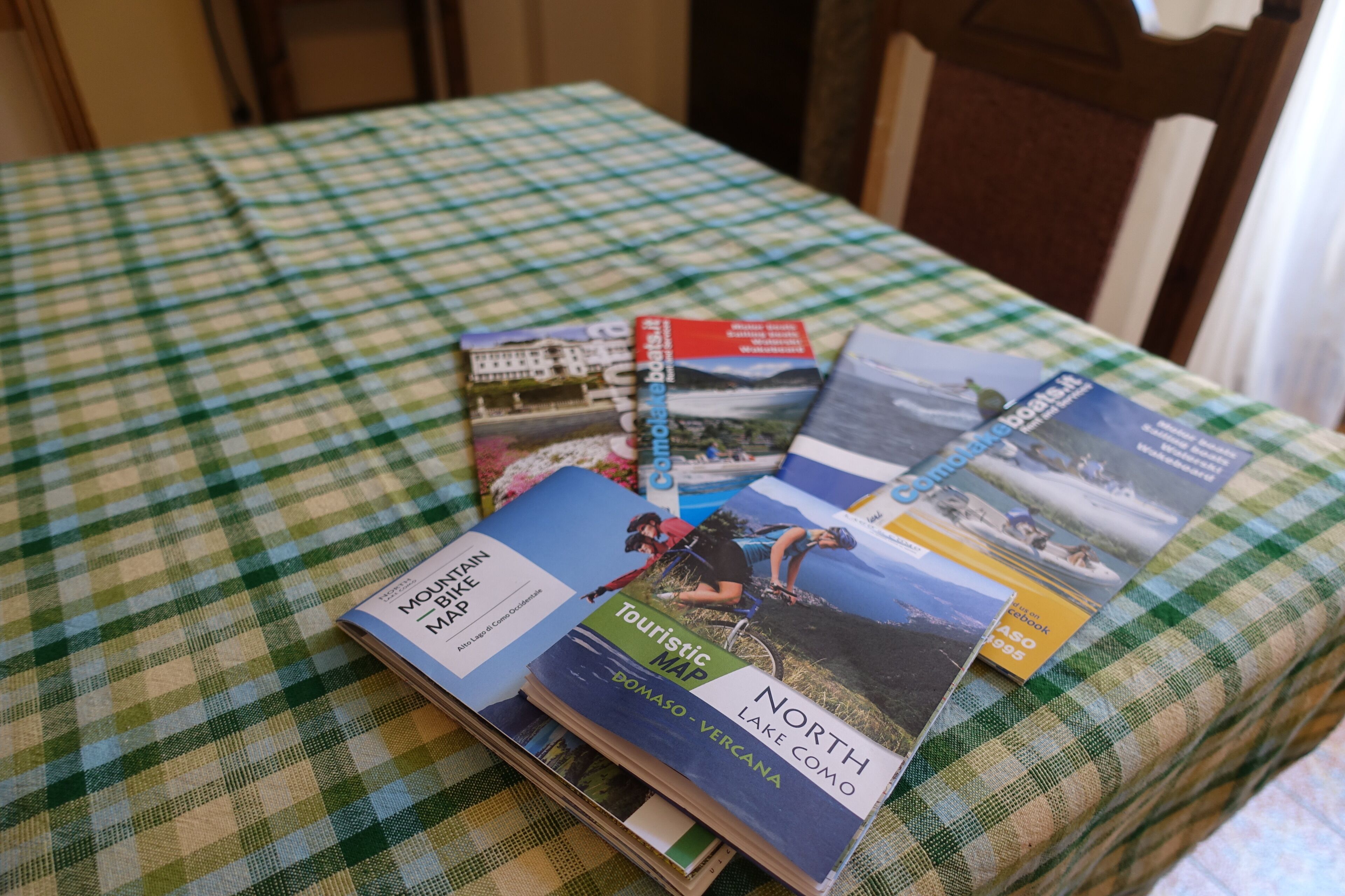 Una mesa con mantel a cuadros y varios mapas y folletos de viaje.