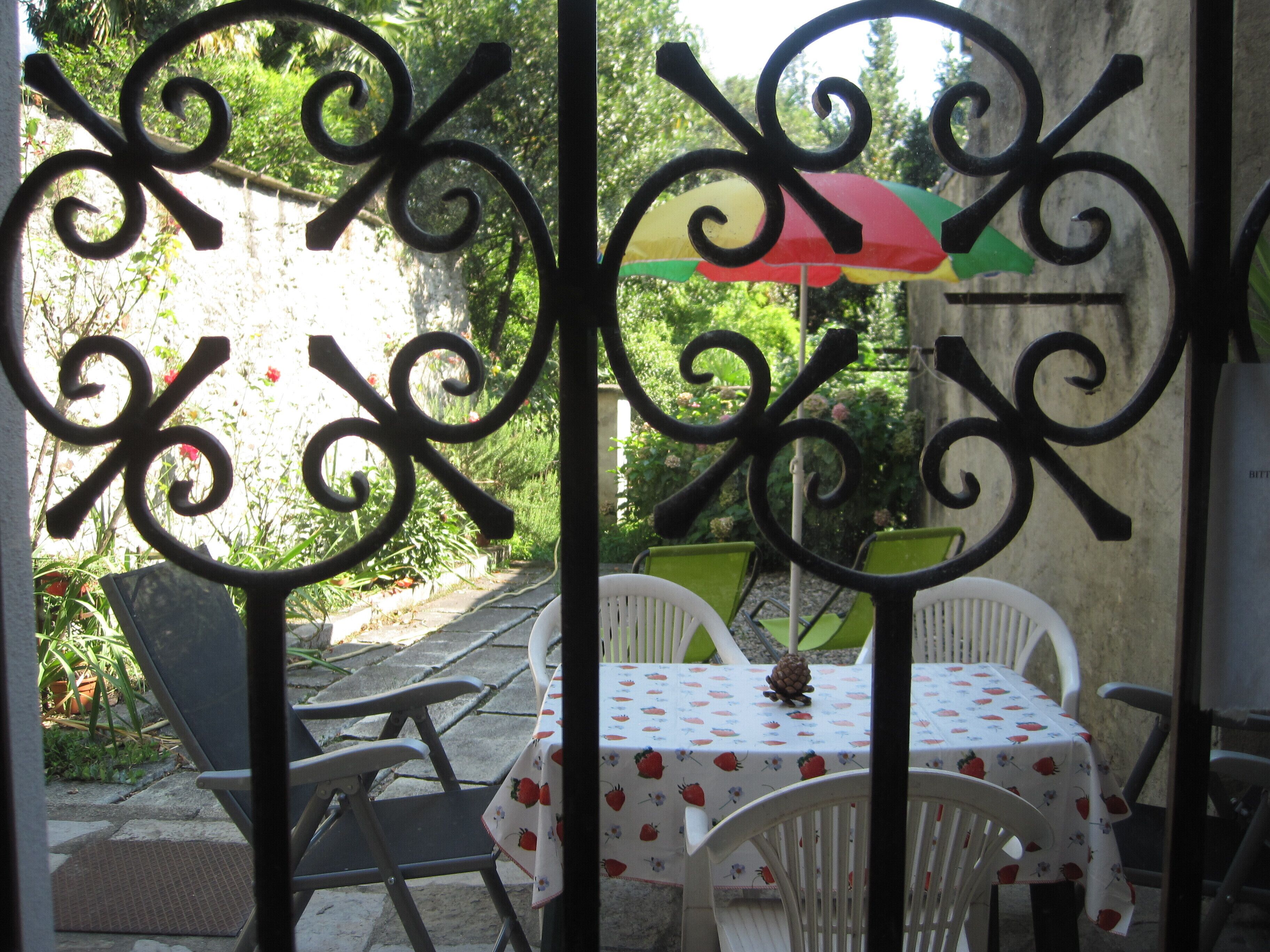 Een terras met een tafel, afgedekt met een tafelkleed met aardbeienprint, omringd door witte stoelen.
