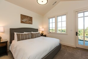 Ein Schlafzimmer mit einem großen Bett, einem Nachttisch mit Lampe, einem Fenster mit Blick auf Grünflächen und einer Deckenleuchte.