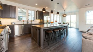 Cuina moderna amb armaris de fusta fosca, electrodomèstics d'acer inoxidable i una illa central amb tamborets.