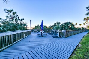 A wooden deck with picnic tables and barbecue grills, surrounded by palm trees and a clear sky. - Luxurious, tropical condo w/panoramic views of the water! (Destin)