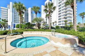 A swimming pool with a 'KEEP OFF' sign, surrounded by palm trees and a white building with balconies. - Luxurious, tropical condo w/panoramic views of the water! (Destin)