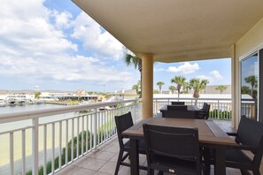 A balcony with a view of a marina, outdoor seating, and a covered area with a table and chairs. - Luxurious, tropical condo w/panoramic views of the water! (Destin)