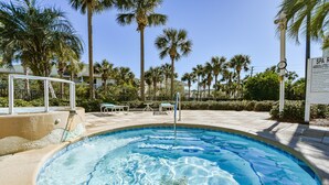 Une piscine avec un jacuzzi, entourée de palmiers et dotée d’un espace de détente.