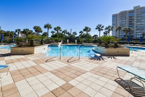 A pool area with tiled flooring, lounge chairs, and palm trees.
