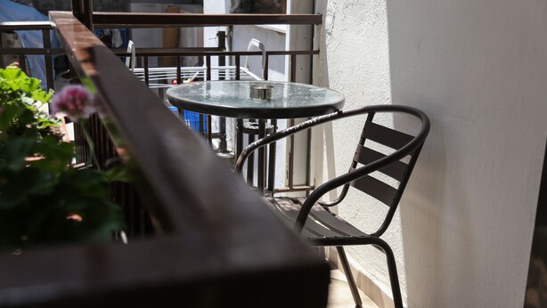 Un balcón con una mesa redonda, una silla, una planta en maceta y una barandilla de metal.