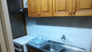 Una cocina compacta con armarios de madera, un lavamanos de acero inoxidable y un microondas.