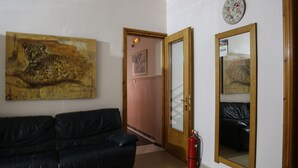 Una sala de estar con un sofá de cuero negro, un cuadro de leopardo, una puerta de madera y un extintor.