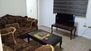 A living room with a brown patterned sofa, a black coffee table with a remote control, and a television on a wooden stand.