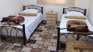 A room with two beds, a small wooden nightstand, a chair, and a window with blinds.