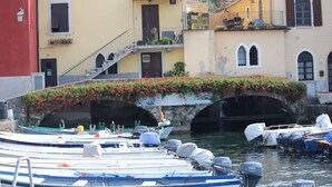 Un canal où sont amarrés des bateaux, un pont orné de fleurs et des bâtiments dotés de balcons.