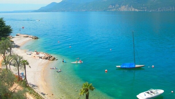 Une plage côtière aux eaux cristallines, avec un rivage sablonneux et un voilier ancré à proximité.